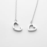 Two silver heart-shaped pendants on a chain against a white background, close-up top down view